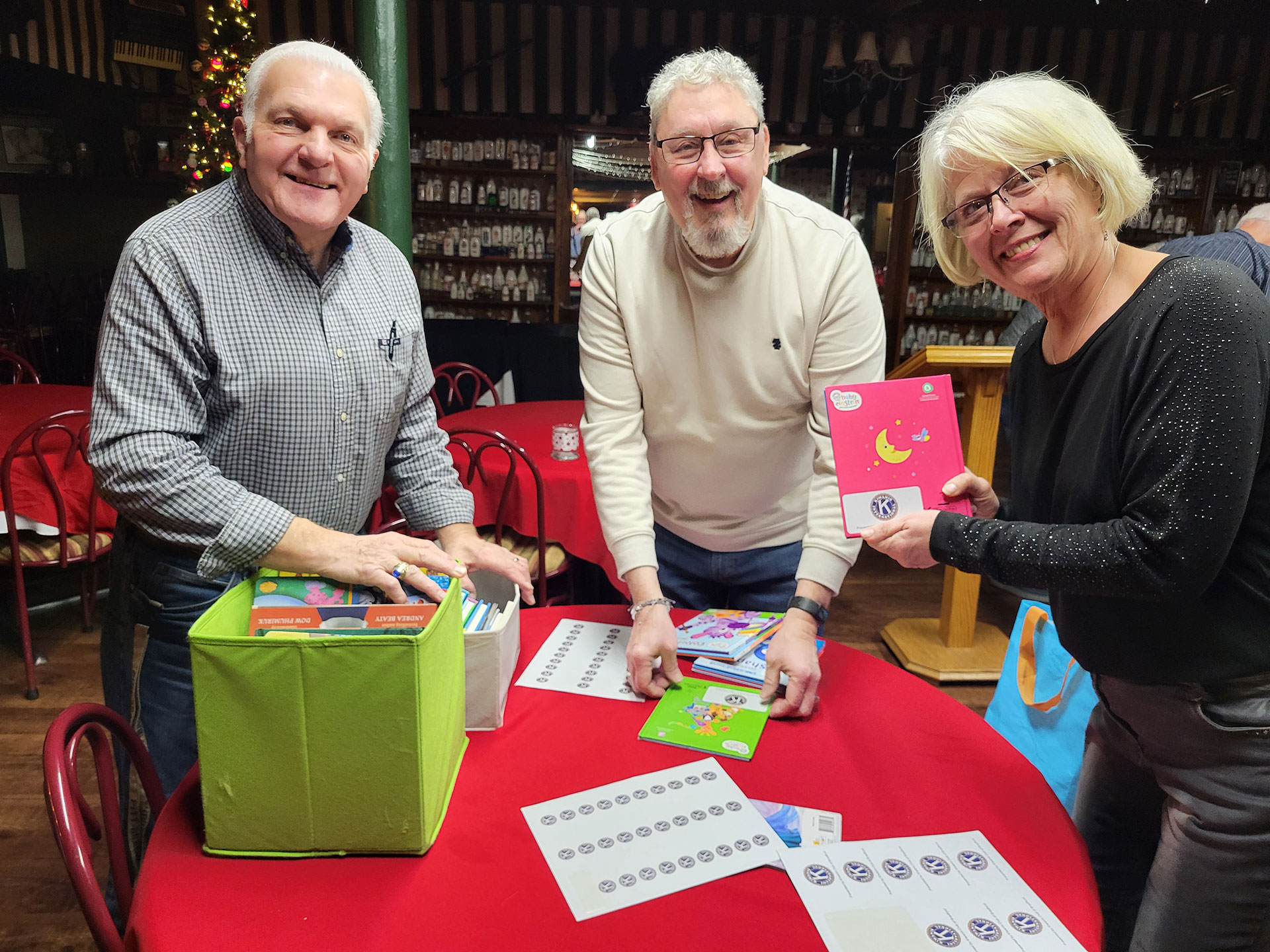 Image of Jerry Harvey, Greg Ulyan and Candy Tingling putting Kiwanis labels into books that we give away at the events we support | Kiwanis Club of Bradford